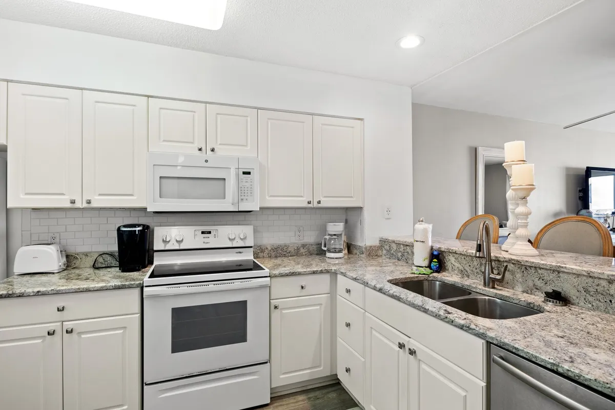 A spacious, modern kitchen featuring granite countertops, white cabinetry, and stainless steel appliances. The kitchen island is central for gathering, and natural light streams in, creating a bright and inviting environment ideal for meal prep and socializing.
