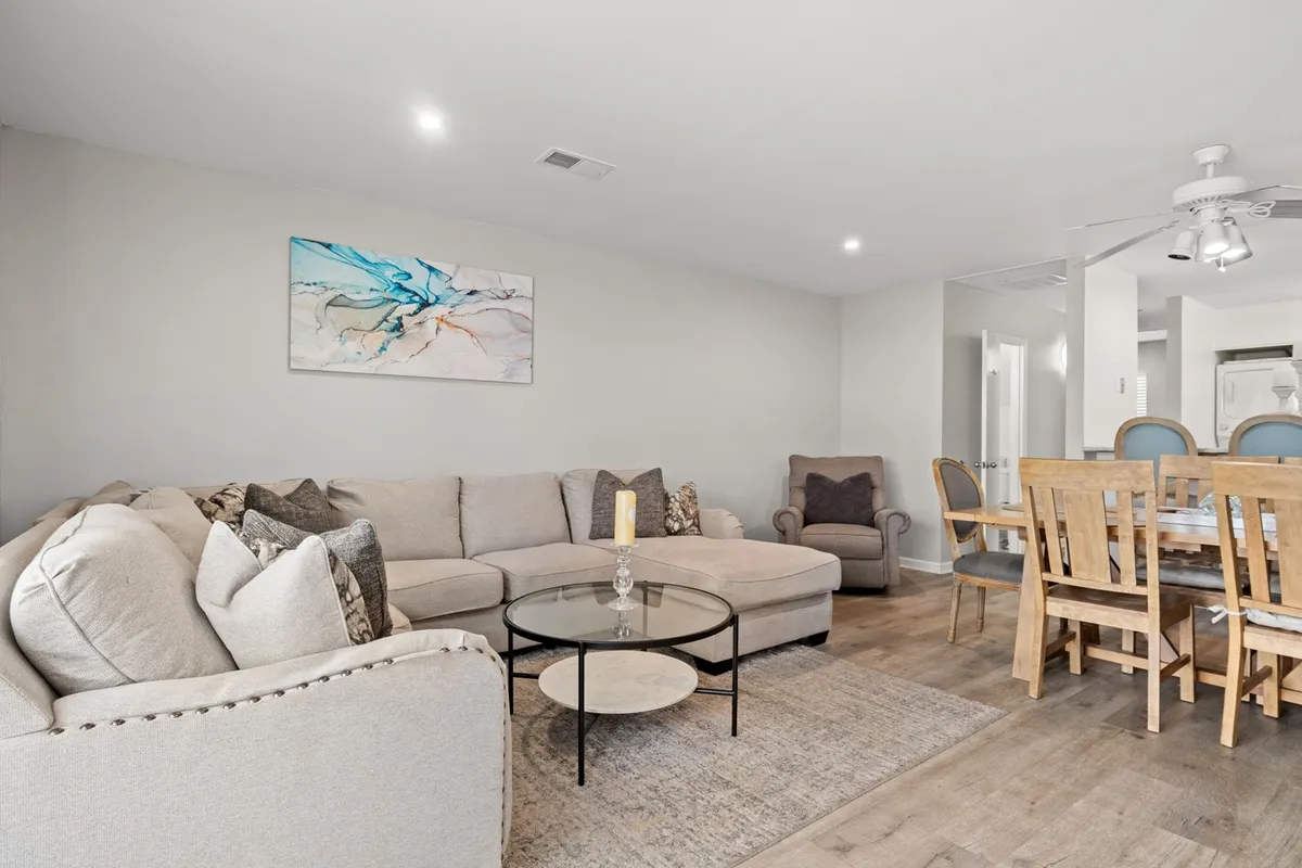 A view of an inviting interior space with a sofa, coffee table, artwork, and a dining table in the background. The mood is warm and comfortable, highlighting spaces for both relaxation and group gatherings.