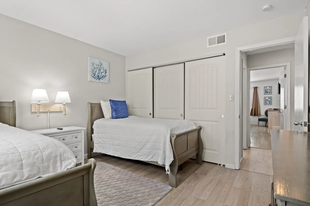A cozy bedroom with two twin beds, a nightstand with a lamp, cheerful blue accents, and decorative wall art. The scene exudes a tranquil and welcoming vibe, perfect for children or friends sharing a room.